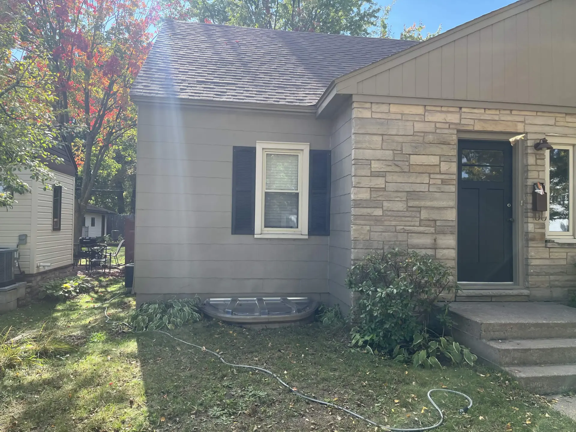 Front of the Weston home after the repaint: khaki gray siding beside the stone entry, cream window trim, black shutters and a dark gray-blue front door.