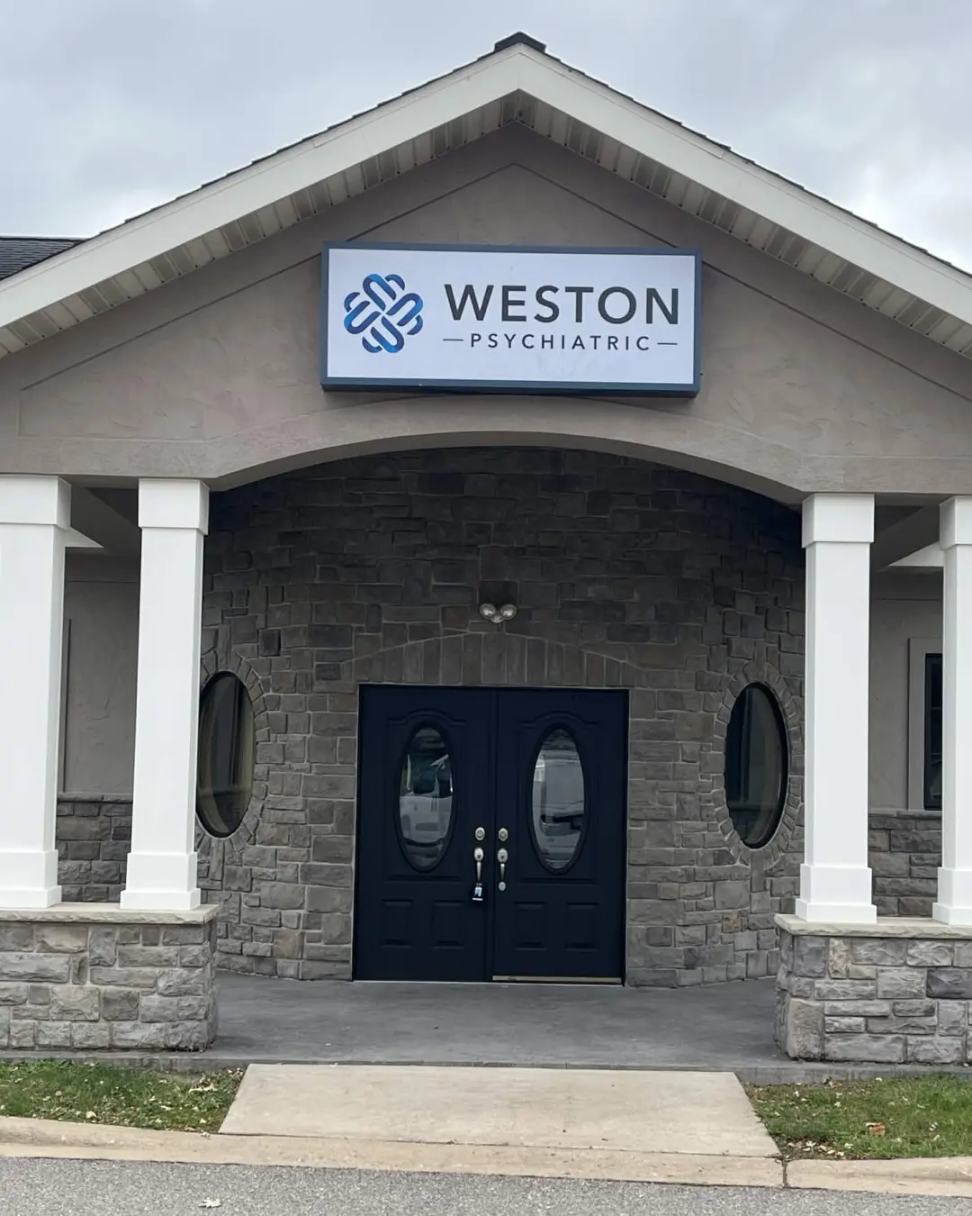 The same entrance after: warm gray stucco, black double doors and black window frames.