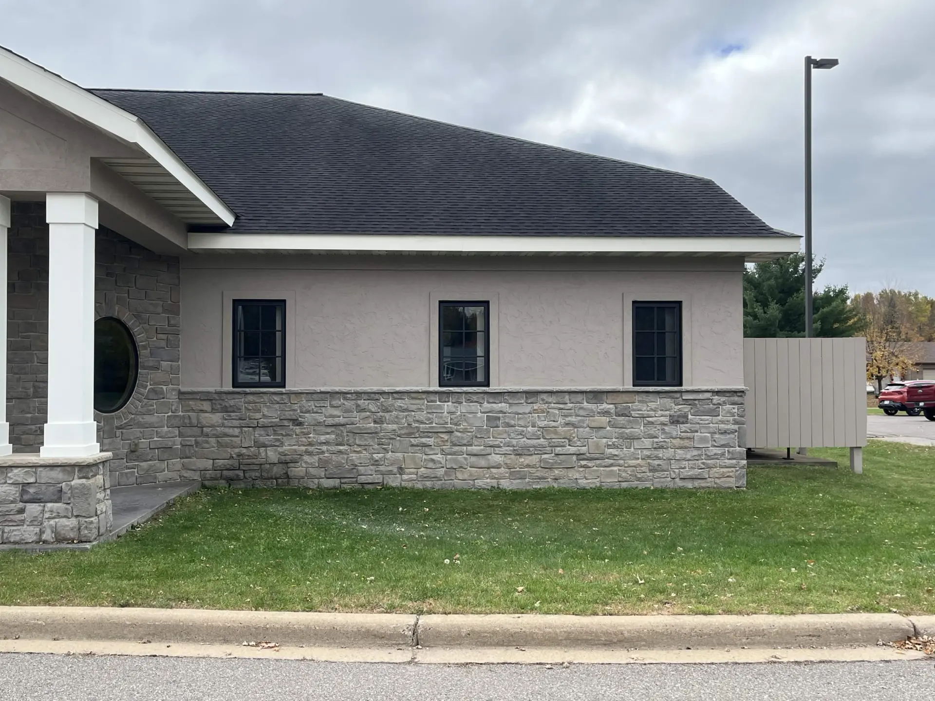 Weston Psychiatric side wall after the repaint, warm gray stucco above stone with black window frames.